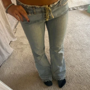 Ljusblå bootcut jeans med snörning - Säljer ett par ljusblå jeans med låg midja och bootcut-ben. Jeansen har snörning framtill istället för vanlig dragkedja och fransiga kanter i midjan. Storlek s/m