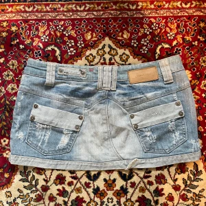 Ljusblå jeanskjol från Soda Brand XS - Ljusblå kort jeanskjol från Soda Brand med slitna detaljer, stora fickor med nitar bak.🌟Midjemått: 39cm Längd: 24cm