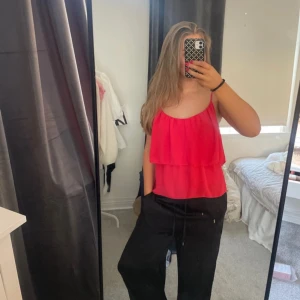 Röd blus med tunna axelband från Bik Bok - Säljer en röd blus från Bik Bok med tunna axelband och lös passform upptill. Perfekt för varma dagar eller sommarens tillfällen.