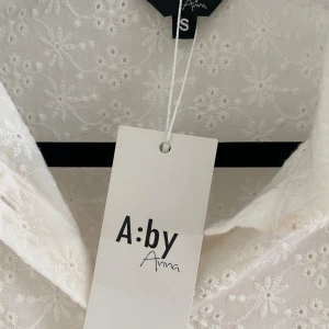 Vit broderad skjorta från A:by Anna - Superfin vit skjorta från A:by Anna med broderade blommor och puffärmar. Skjortan har klassisk krage, knäppning framtill och korta ärmar med resår. Perfekt för en fräsch och somrig look!