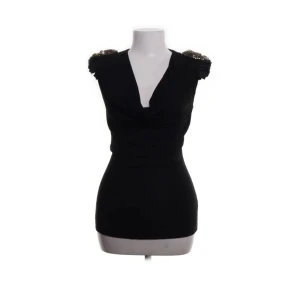 Svart topp med pärldetaljer Robert Rodriguez - Supersnygg svart topp från Robert Rodriguez med pärldetaljer på axlarna och djup v-ringning. Modellen är tight och ärmlös, perfekt för dig som vill sticka ut. Materialet känns mjukt och följsamt mot kroppen. En riktig statement-piece för din garderob!