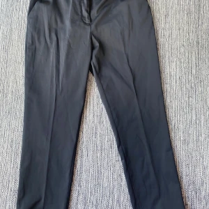 Svarta kostymbyxor Day Birger et Mikkelsen - Stilrena svarta kostymbyxor från Day Birger et Mikkelsen. Byxorna har rak passform, diskreta fickor och är tillverkade i en mjuk mix av rayon, polyester och lite stretch för extra komfort. Perfekta till en snygg och clean look.