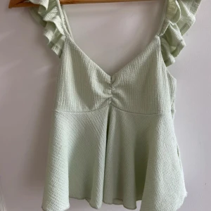 Ljusgrön linnetopp från gina  - Säljer en supersöt ljusgrön linnetopp med volangprydda axelband och v-ringning. Perfekt till sommaren och vinter med en kofta över! Kommer inte till användning, ny utan prislapp💚