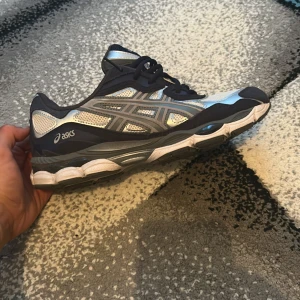 Asics sneakers i silver och marinblå - Snygga Asics sneakers i silver, vitt och marinblått med meshpaneler och reflekterande detaljer. Skorna har klassisk snörning, rund tå och en bekväm, dämpad sula. Perfekta för dig som gillar sportig stil och vill ha något som sticker ut.