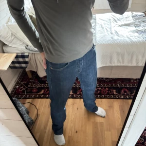 Levi's 501 blå jeans straight fit - Klassiska blå Levi's 501 jeans med rak passform och normal midja. Jeansen har fem fickor, synliga nitar och är tillverkade i slitstarkt denim. Perfekta för dig som gillar en tidlös och avslappnad look.
