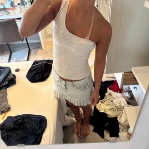 Vit oneshoulder topp med strukturmönster - Säljer en vit oneshoulder topp med snygg struktur och mönstrad yta. Toppen är ärmlös och har en asymmetrisk axel, vilket ger en modern och trendig look. Perfekt till sommarens outfits och lätt att matcha med kjol eller jeans.