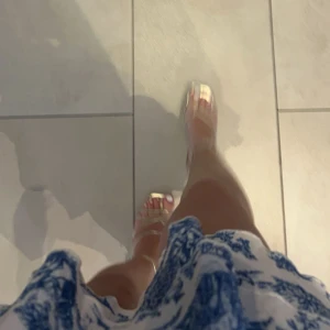 Vit och blå axelbandslös kortklänning - Superfin axelbandslös kortklänning med volangkjol och romantiskt blått mönster på vit botten. Klänningen har en figurnära överdel och är perfekt för sommarens alla tillfällen. Materialet är mjukt och har en lätt struktur.