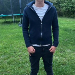 Mörkblå stickad kofta från BOSS - Säljer en mörkblå stickad kofta från BOSS med dragkedja framtill och hög krage. Koftan har långärmad passform och ribbade muddar. Perfekt för lager-på-lager och snygg till jeans eller chinos.