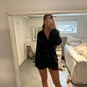 Svart omlottklänning med v-ringning från Zara  - Snygg svart kortklänning med omlott och djup v-ringning. Klänningen har långa ärmar och en figurnära passform med lätt rynkade detaljer i midjan. Perfekt för dig som vill ha en stilren och trendig look. 