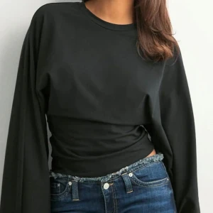 Svart långärmad tröja - En svart långärmad tröja med enkel design och rund halsringning. Tröjan har en tight passform över midjan och är perfekt att matcha med höga jeans. Materialet känns mjukt och stretchigt, vilket gör den bekväm att bära. Den har breda armar. Använd 1 gång, säljs då den inte passade bra på mig 