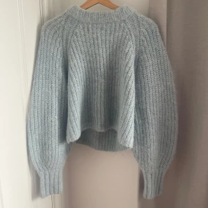 Ljusblå stickad tröja från H&M - Supermysig ljusblå stickad tröja från H&M i alpackablandning. Tröjan har en loose passform, breda ärmar och ribbade muddar. Perfekt för kyliga dagar när du vill vara både varm och snygg.