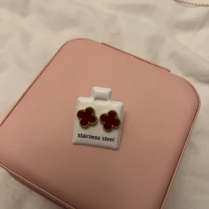 Röda klöverformade örhängen i guld - Snygga örhängen i klöverform med röd mitt och guldfärgad kant. Tillverkade i stainless steel, perfekta för dig som vill ha något unikt och färgglatt. Passar dig som gillar att sticka ut med coola detaljer.