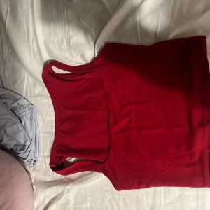 Röd ärmlös linnetopp - En enkel och stilren röd linnetopp med klassisk rak passform och breda axelband. Perfekt att matcha med jeans eller kjol för en snygg och avslappnad look. Toppens material känns mjukt och följsamt mot huden.