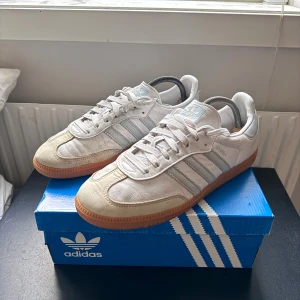 Adidas samba skor - Klassiska Adidas Samba sneakers i vitt skinn med ljusgrå detaljer och gummisula. Ikoniska tre ränder på sidan, snörning och låg profil. Perfekta för dig som gillar retrostil och streetwear. 