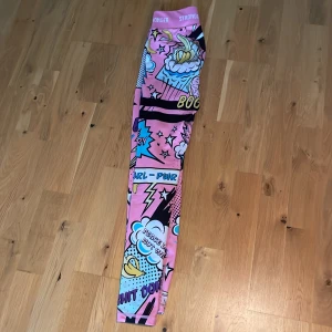 Färgglada leggings från Stronger XS - Säljer ett par sjukt coola leggings från Stronger i storlek XS. De har ett färgstarkt pop art-mönster med rosa, blå, svart och gula detaljer samt text och blixtar. Materialet är stretchigt med 85% polyester och 15% elastan, perfekt för träning eller chill. Fick dom i julklapp för ungefär 1 år sen men har inte använt dom en ända gång. Sitter jätte skönt och är väldigt häftiga. Men säljer då jag tror att någon annan skulle ha större användning av dem! 
