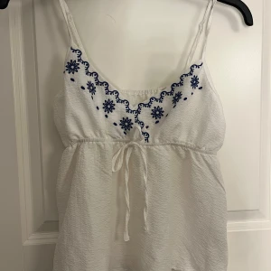 Vit kort sommarklänning med broderi - Supersöt vitt linne med blått blommigt broderi vid bröstet 