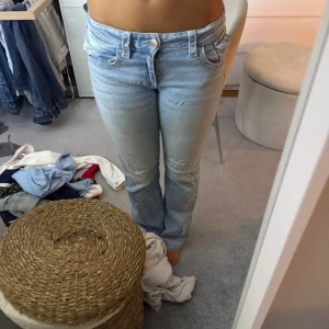 Ljusblå bootcut jeans med låg midja - Säljer ett par ljusblå jeans med bootcut-snitt och låg midja. Jeansen har klassiska fem fickor, snygga detaljer vid fickorna och stängs med knapp och dragkedja. Perfekta för dig som gillar en avslappnad men ändå trendig look. Har sytt i rumpan då det sprack där