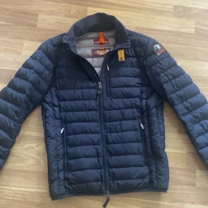 Parajumper jacka  - Snygg mörkblå dunjacka från Parajumpers med quiltad design, hög krage och gul detalj vid halsen. Jackan har dragkedja framtill, två sidofickor med dragkedja och patch på ena ärmen. Perfekt för kyliga dagar och riktigt stilren look. Inte mycket använd och är i fint skick. 