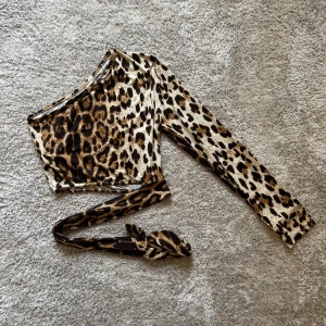 Leopardmönstrad oneshoulder topp  - Säljer en riktigt cool leopardmönstrad oneshoulder topp från SHEIN i storlek S. Toppen har lång ärm på ena sidan och ett knytband i midjan. Materialet är mjuk och stretchig polyester