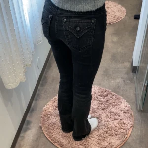 Svarta jeans från Miss Me, bootcut - Säljer ett par svarta jeans från Miss Me med snygga detaljer på fickorna och dekorativa knappar. Jeansen har låg midja och bootcut-snitt, vilket ger en schysst siluett. Materialet är klassisk jeans och de har coola sömmar som sticker ut.