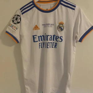 Real Madrid tröja 21/22 - Real Madrid tröja från 21/22 säsongen med Champions league märke och final detaljer från Champions league finalen 2022 Paris. Priset går att diskuteras