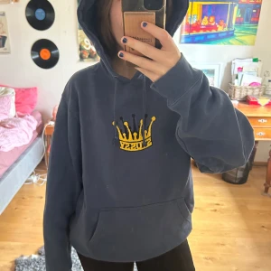Mörkblå Stussy hoodie med krona - Säljer en mörkblå hoodie från Stussy i storlek M. Tröjan har en gul broderad krona med Stussy-loggan på bröstet, huva med snörning och en stor magficka. 