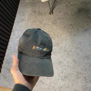 Astroworld keps - Säljer en svart keps från Astroworld med färgglad broderad logga framtill och texten 'Wish You Were Here' broderad baktill. Justerbar rem med metallspänne för perfekt passform. Kepsen är i mjuk bomull och har klassisk böjd skärm.