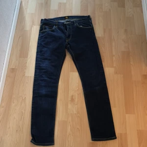 Mörkblå Lee Luke jeans W31 L32 - Snygga mörkblå jeans från Lee, modell Luke. Klassisk femficksdesign med Lee-läderpatch bak och kontrastsömmar. Jeansen har en smal passform och är tillverkade i slitstarkt denimtyg. Perfekta för dig som gillar en stilren och modern look.