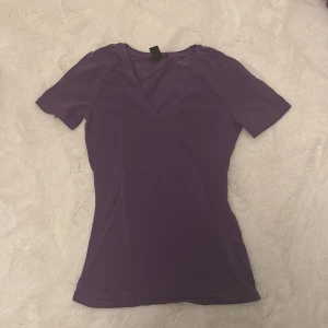 Lila v-ringad t-shirt från Amisu - Snygg lila t-shirt från Amisu i storlek XS. Modellen är figurnära med korta ärmar och v-ringad hals. Tillverkad i mjuk bomull som känns skön mot huden. Perfekt att matcha med jeans eller shorts för en chill look.