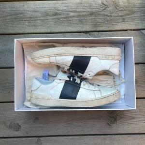 Valentino Open sneakers vit/svart - Snygga Valentino Garavani Open sneakers i vitt skinn med bred svart läderdetalj över sidan och coola nitar baktill | Storlek: 42 1/2 | Snörerna är utbytta!🤝🏻Man får med original låda och påse✅Perfekta för dig som gillar stilrena men ändå unika sneaker!🔥👟Släpper billigt då de inte är äkta😉‼️Skriv om ni har någon fråga prisförslag!🫡