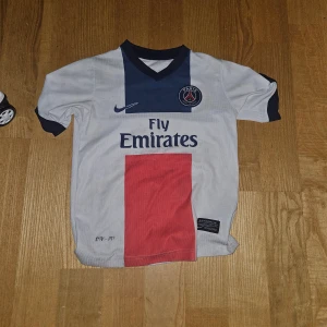 PSG Ibrahimovic #10 fotbollströja Nike - Paris Saint-Germain fotbollströja med Ibrahimovic och nummer 10 på ryggen. Tröjan är vit med mörkblå detaljer, röd vertikal panel på framsidan och PSG-logga på bröstet. Kortärmad med V-ringad krage, tillverkad i lätt funktionsmaterial.