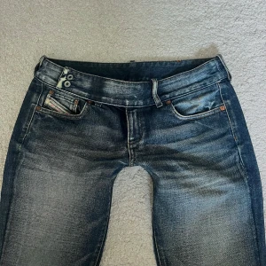 Lågmidjade Diesel jeans  - Blåa lågmidjade jeans från Diesel med dubbla knappar i midjan. Jeansen har rak passform och är tillverkade i slitstarkt denim. Midjemåttet är 39 cm och innerbenslängden är 78 cm 🩷 
