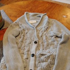 Ljusgrå kofta från These Glory Days - Säljer en ljusgrå stickad kofta från These Glory Days i storlek small. Koftan har snygg kabelstickad framsida, stora knappar och en liten ficka. Perfekt för lager-på-lager och chill höst- eller vinterstil.