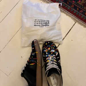 Maison Martin margiela - Tja. Säljer mina Maison margiela sneakers i svart färg med färg stänk. Haft dom i ett tag men gillar de inte super mycket. Priset är ej hugget i sten. Hör av er vid frågor!!😊