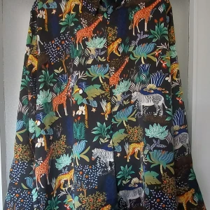 Arabella skjorta med djungelmönster - Unik skjorta från Arabella med färgstarkt djungelmönster som visar giraffer, zebror och leoparder bland gröna och blå blad. Skjortan har svart botten, klassisk krage och knappar framtill samt vid ärmslut. Perfekt för dig som gillar att sticka ut med coola prints.