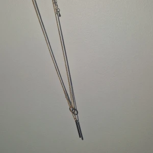 Guldigt halsband - Snyggt halsband i guldton med två tunna kedjor och ett stilrena hängsmycken i form av en liten stav och en cirkel. Perfekt för dig som gillar enkel och modern design. Justerbar längd med klassisk kedjelänk. Passar till alla dina outfits.
