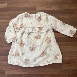 Blommig tröja - Supersöt vit tröja från Newbie i storlek 62 (2-4mån). Sparsamt använd och helt utan anmärkningar. Knappar i ryggen.