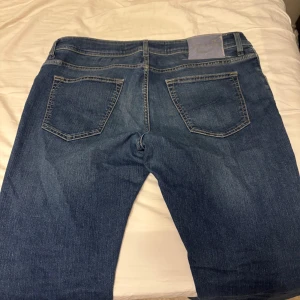 Blå jeans från Jacob Cohen - Snygga blå jeans från Jacob Cohen med klassisk femficksdesign och kontrastsömmar. Jeansen har en rak passform och är tillverkade i mjukt denimtyg av hög kvalitet. Perfekta för dig som gillar stilrena och tidlösa jeans med italiensk känsla. Storleken är 36 skulle säga att de lite mindre de sitter lite stort på mig jag har vanligtvis runt 34 men dessa funkar ok de är  lite stora 