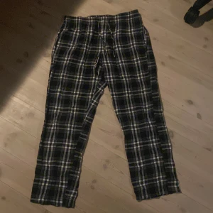 Svarta rutiga byxor med snörning - Säljer ett par svarta byxor med vitt och svart rutmönster och snörning i midjan. De är mjuka och sköna, perfekta för att chilla hemma eller till vardags. Klassisk rak passform och elastisk midja för extra komfort.