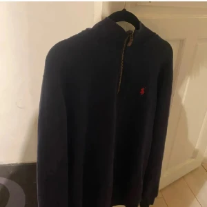 Marinblå half zip tröja från Polo Ralph Lauren - Snygg marinblå långärmad tröja från Polo Ralph Lauren med half zip och röd broderad logga på bröstet. Tröjan har en hög krage och är gjord i mjuk bomull, perfekt för chill dagar. Passar dig som gillar klassisk stil med en modern touch.