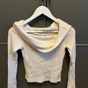 Ljusbeige ribbad tröja Gina Tricot - Supersnygg ljusbeige ribbad tröja från Gina Tricot med bred krage och lång ärm. Tröjan är croppad och har en tight passform som framhäver figuren. Perfekt att styla med höga jeans eller kjol.