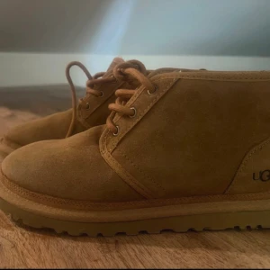 Bruna mockaboots från UGG - Säljer ett par klassiska bruna boots från UGG i mjuk mocka med snörning och grov sula. Perfekta för höst och vinter, med en stilren och enkel design som funkar till det mesta. UGG-logga på hälen och rund tå för en avslappnad vibe.
