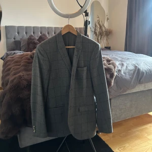 Grå rutig kavaj från Tiger of Sweden - Snygg grå kavaj från Tiger of Sweden med rutigt mönster. Klassisk passform med två framfickor, bröstficka och knappar vid ärmslut. Perfekt för dig som gillar stilrena och tidlösa plagg. Materialet känns mjukt och exklusivt.