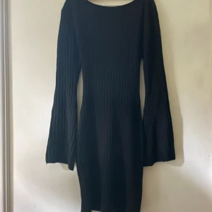 Svart ribbad klänning med öppen rygg - Svart stickad ribbad klänning med vida ärmar och snygg öppen rygg. Superskönt och sticks inte alls, relativt tajt i passformen. Strl S