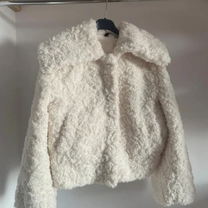 Vit teddyjacka med stor krage - Supermysig vit teddyjacka med oversized krage och lång ärm. Jackan är fluffig och har en cool, lite boxig passform. Perfekt för att hålla sig varm och ändå se trendig ut. Stängs med dragkedja och har ett riktigt mjukt teddy-material.