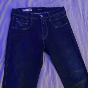  Replay jeans W29 L32 - Säljer ett par mörkblå Replay Anbass jeans med klassisk femficksdesign och snygga kontrastsömmar. Modellen har normal passform och raka ben, perfekt för dig som gillar stilrena och tidlösa jeans. Materialet är mjukt och stretchigt för extra komfort.