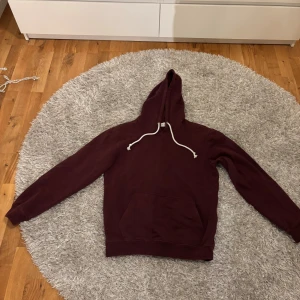 Vinröd hoodie från Pier One - Säljer en vinröd hoodie från Pier One med klassisk känguruficka och vit snörning i huvan. Tröjan har lång ärm och är tillverkad i mjuk bomull, perfekt för chill dagar. Enkel och stilren design som funkar till det mesta.