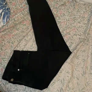 Svarta slim fit jeans från H&M - Svarta slim fit jeans från H&M med klassisk femficksdesign och raka ben. Jeansen har silverfärgade nitar och knapp, samt en diskret etikett på insidan. Snygg passform som sitter tajt men ändå bekvämt. Perfekta till en stilren look.