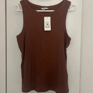 Ribbat brunt linne från Cubus  - Säljer en ribbad brun linnetopp från C i storlek L. Toppen är ärmlös med rund halsringning och har en snygg, enkel design som är lätt att matcha. Materialet är mjukt och stretchigt, perfekt för dig som gillar bekväma och stilrena plagg.