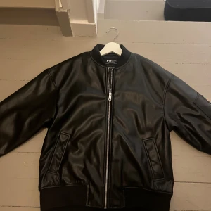 Svart jacka i skinnimitation   - Snygg svart jacka från New Yorker i skinnimitation med ribbad mudd vid ärmslut och midja. Jackan har dragkedja framtill, två snedställda fickor och en stilren look som passar perfekt till typ vad som helst. Fodrad insida för extra komfort. Aldrig använd.😁